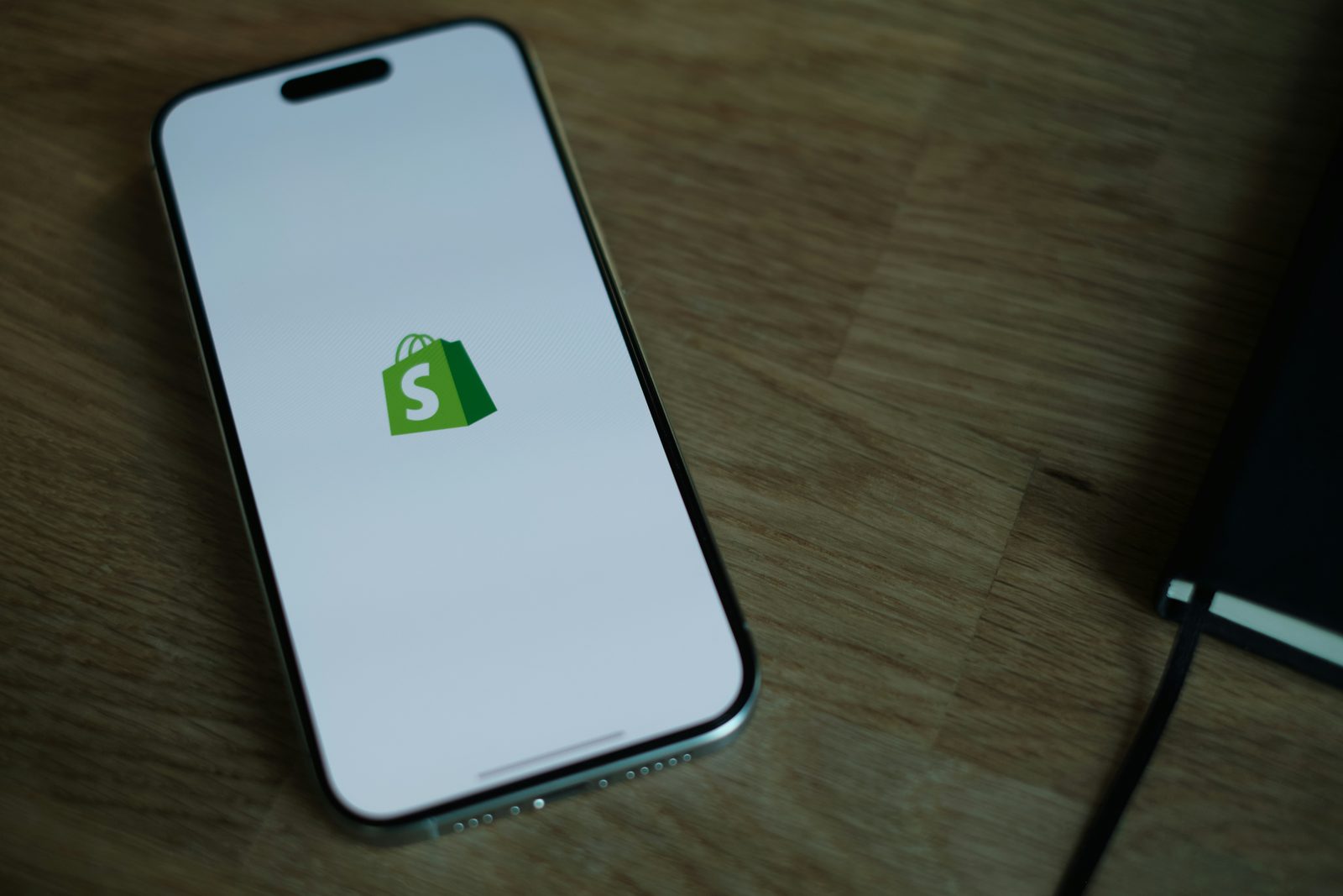 Smartphone affichant le logo Shopify, posé sur un bureau en bois